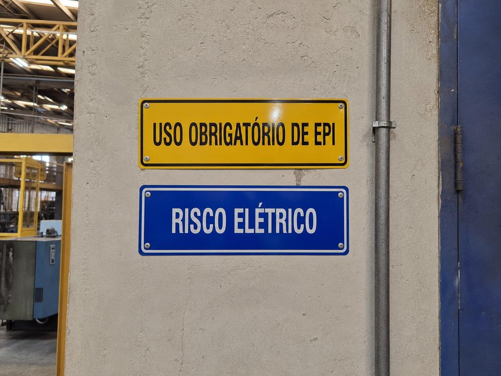 Placas de uso obrigatório de EPI e risco elétrico em parede industrial